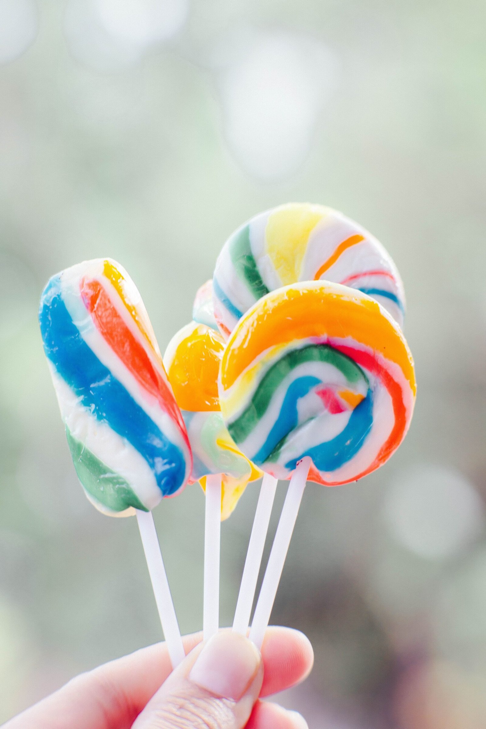 Colorful lollipops held up against a blurred outdoor background, showcasing vibrant swirls.