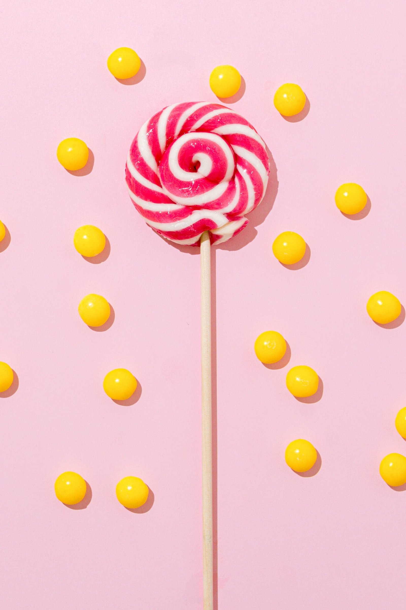 Bright lollipop and yellow candies arranged on a pink surface offering a vibrant and fun visual.